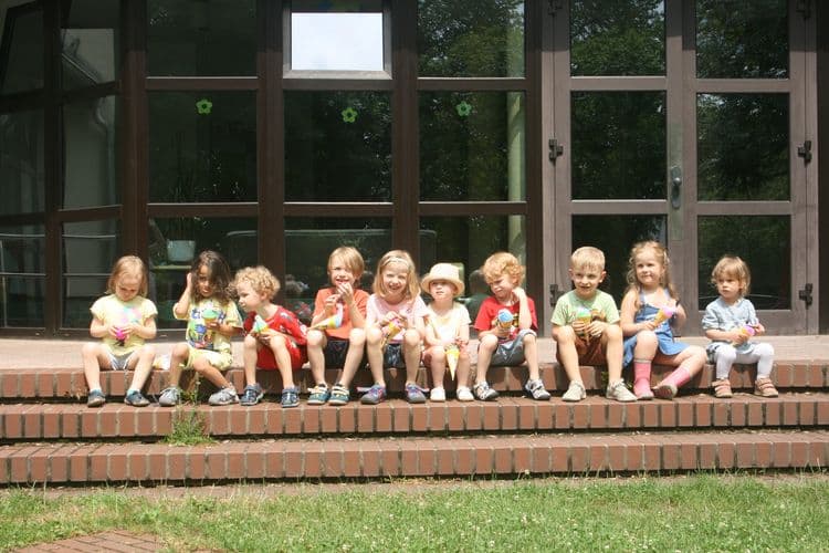 Zehn Frohe Herrgottstunde-Kinder im Alter von 2 bis 6 Jahren sitzen auf einer dreistufigen Treppe nebeneinander.