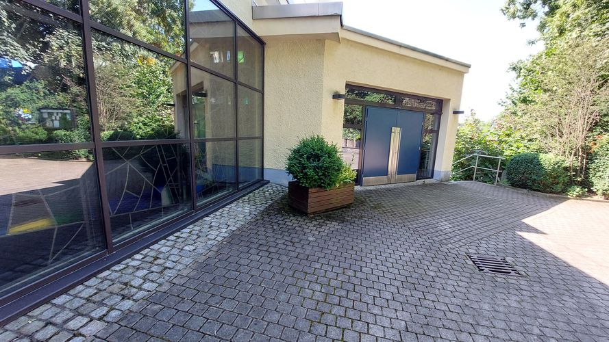 Der gepflasterte Platz vor dem Kircheneingang, links davon ein großes Bleiglasfenster