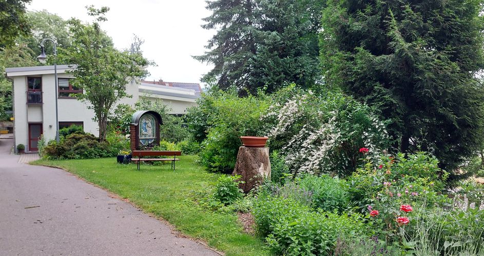 Der Weg zur Kirche mit Blumen und Marienrelief am Rand